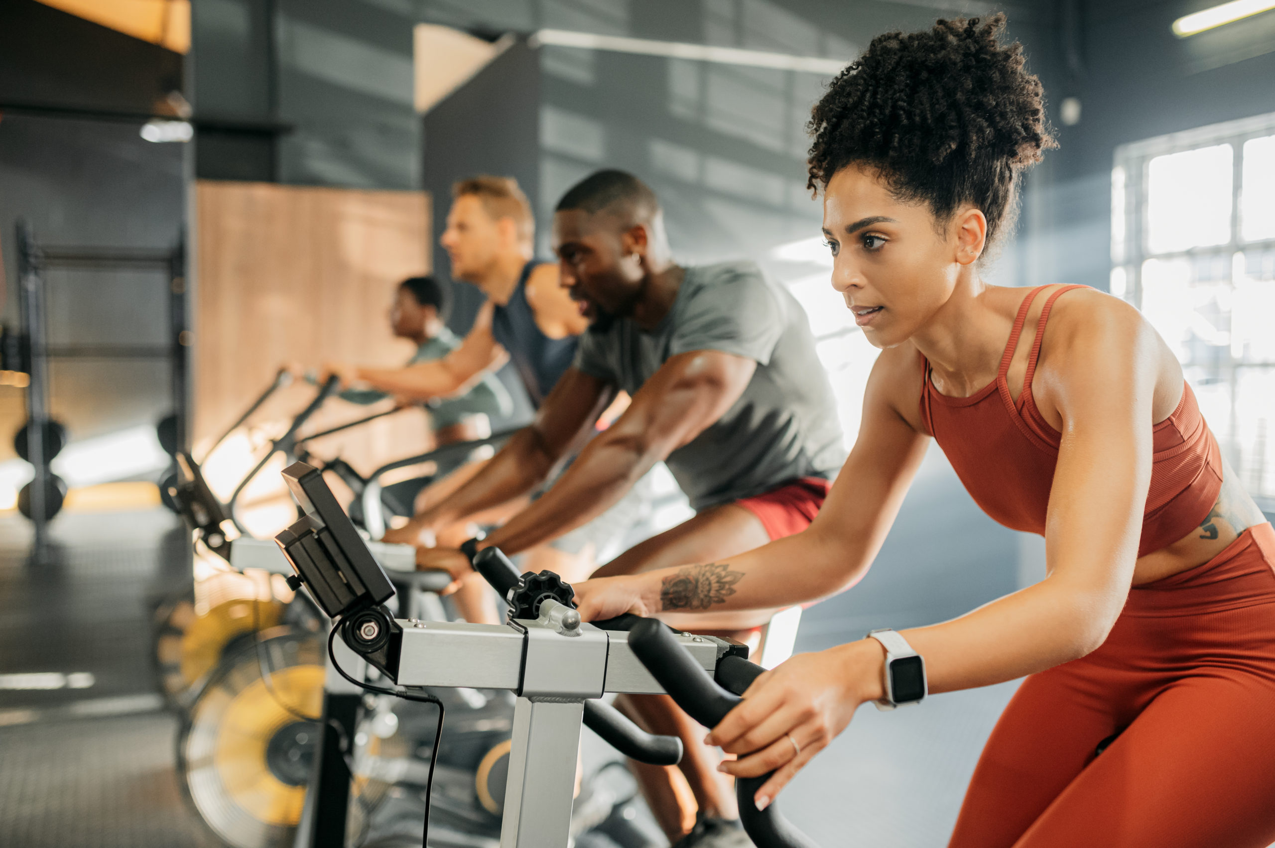 A black woman with group on exercise bike, cycling at gym to lose weight and improve cardiovascular fitness health. A bicycle is the best activity for cardio, healthy fat loss and training for sports Biking Soft