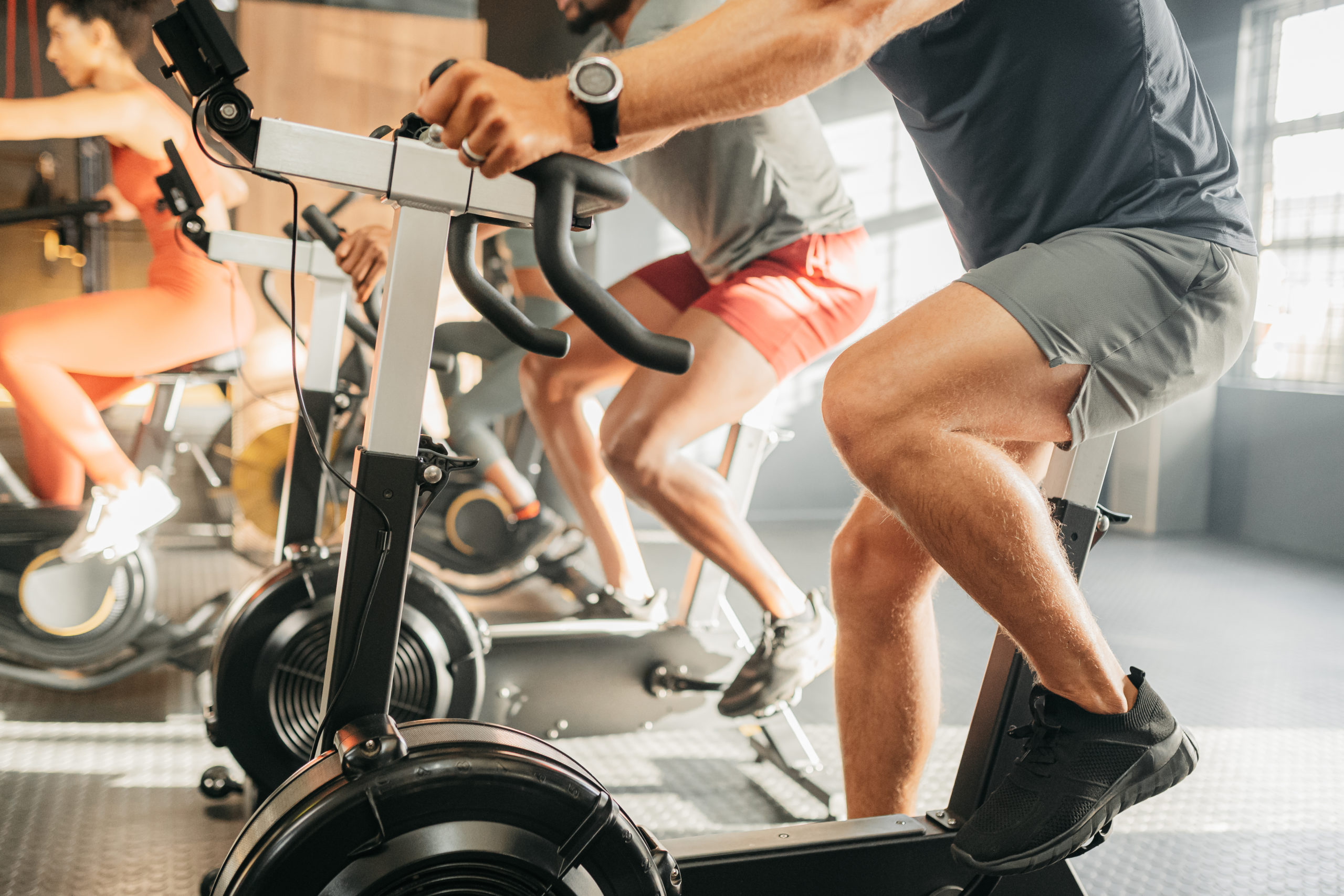 Legs of group exercise bike machine in gym, running shoes and workout apparel. Cycling helps cardiovascular health, body fitness and sports training. Friends workout class together, compete and grow Biking Soft