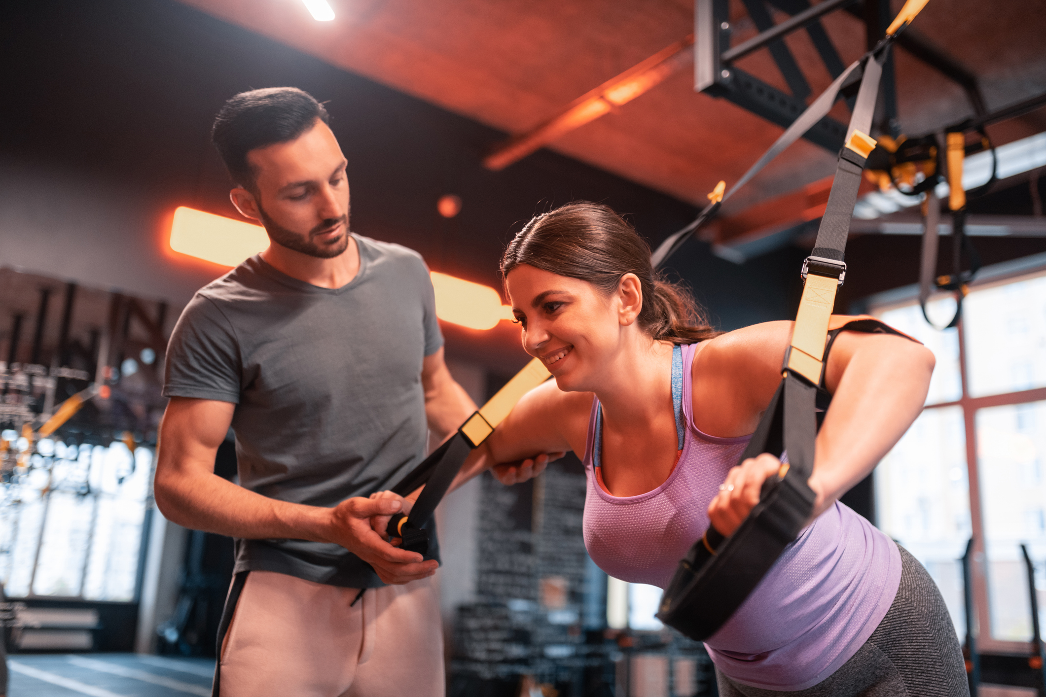 Fitness trainer assisting plump woman exercising on TRX personal coaching